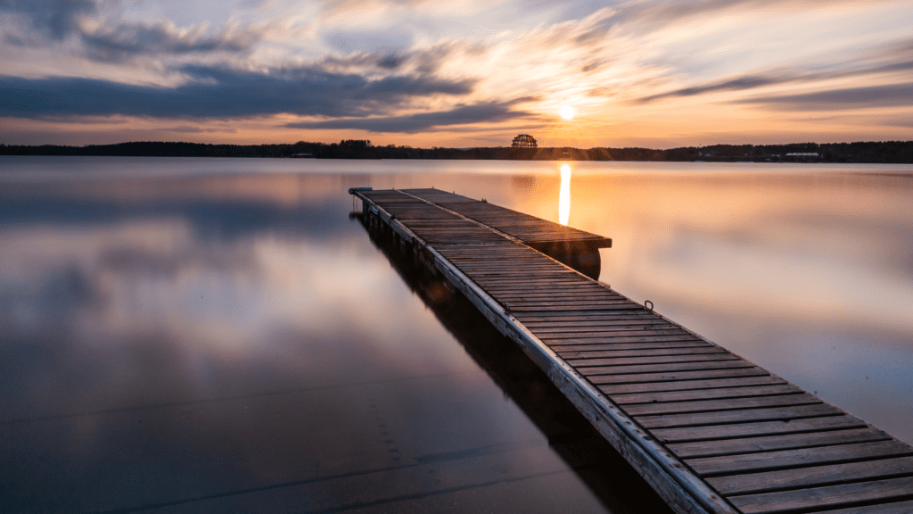 A wooden pontoon on a calm lake at sunset. The image depicts a feeling of tranquillity and calm.