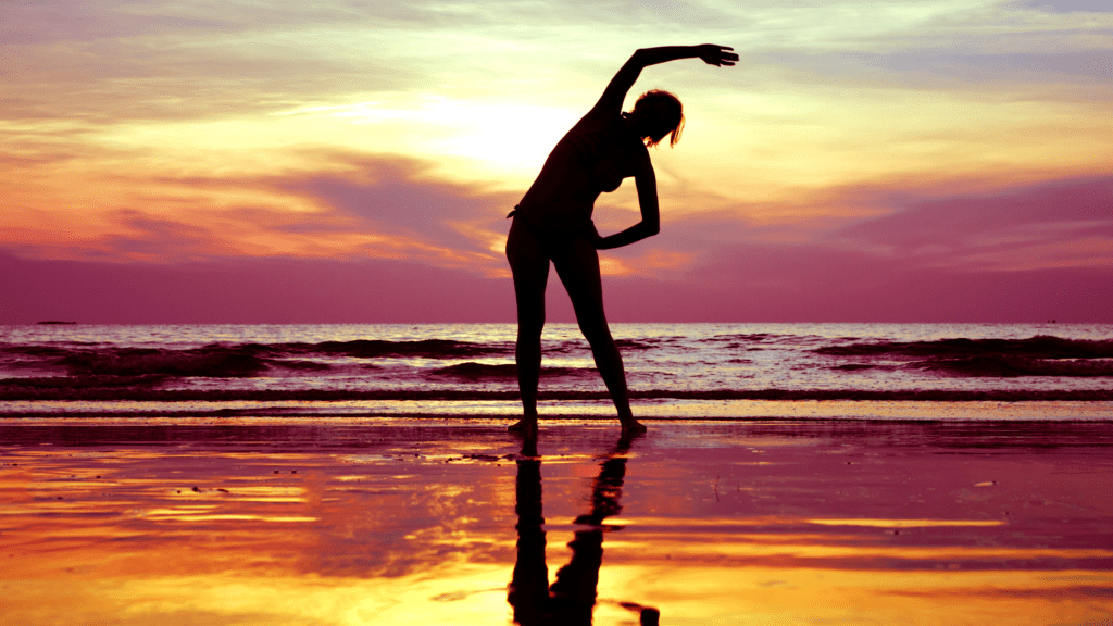 Silhouette of a person exercising on a beach at sunset.