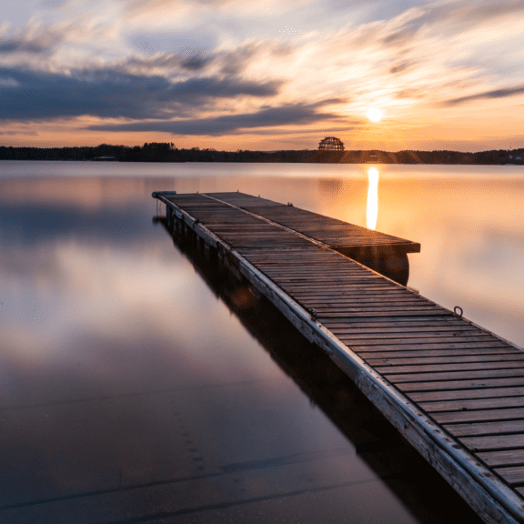 A wooden pontoon on a calm lake at sunset. The image depicts a feeling of tranquillity and calm.